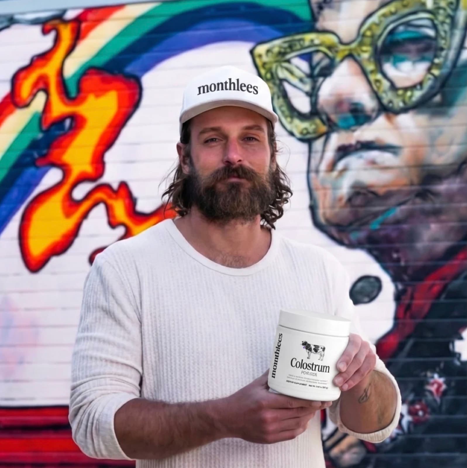 Christopher Walker in front of a mural, holding Monthlees Colostrum
